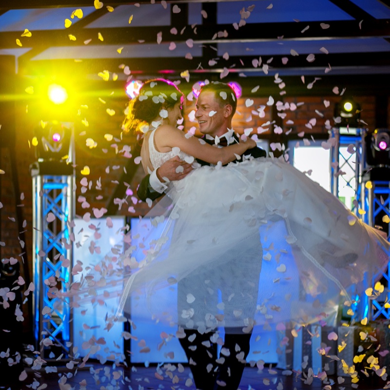 Pan młody niesie na rękach swoją nowo poślubinoną żonę wsród confetti